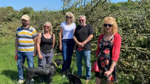 BBC Five people stood in front of felled trees in Higham. Two have dogs.