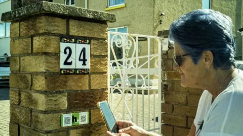 HistoryPoints.org Rhyl house with woman scanning QR code of HistoryPoints.org plaque