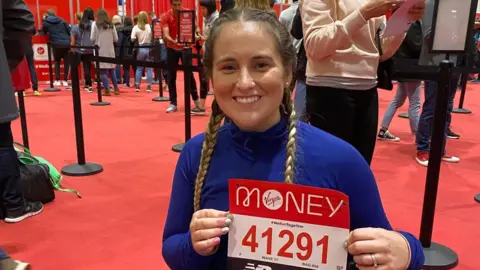 Spinal Injuries Assocation A women in a wheelchair holding a race number up smiling at the camera 