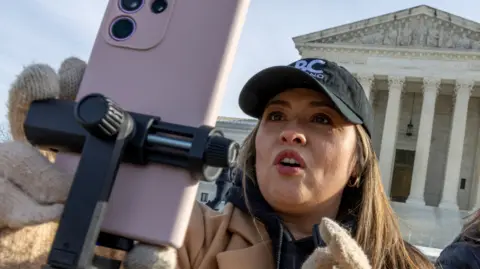 A woman holding a phone on live stream in front of the Supreme Court 