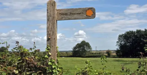 BBC A wooden sign in a field that says 'public footpath'