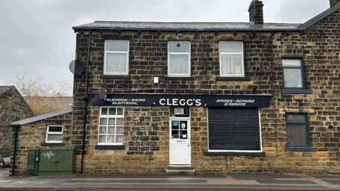 Julia Bryson/BBC An electrical shop in a Yorkshire stone building with a sign which reads Clegg's. There are net curtains at the window and the stone is black from soot. 