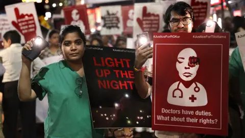 EPA Crowds protesting in India. One person holds a banner saying: "Doctors have duties. What about their rights?" Another holds a poster saying: "Light up the night."