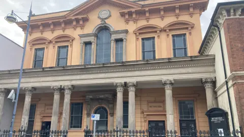 The exterior of a historic Victorian Methodist chapel with ornate columns and an orange frontage. There are large windows on both of the building's two storeys.