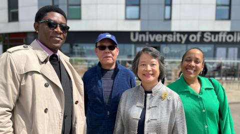 Four people of different ethnicities stand together outside a university building