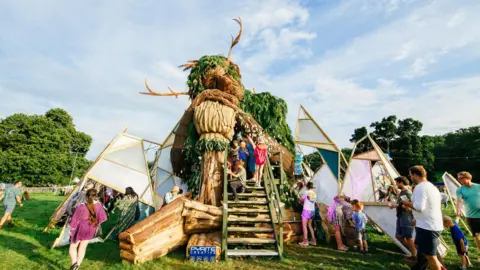 Nici Eberl Families and children explore a large sculpture of a Green Man