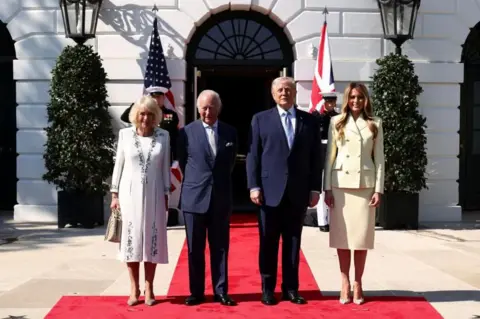 Reuters U.S. President Donald Trump and first lady Melania Trump pose for a picture with Britain's King Charles and Queen Camilla, all dressed formally, standing on a red carpet in front of two saluting soldiers