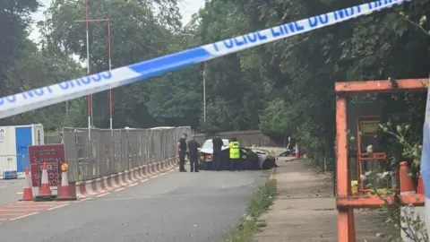 A police car and a crime scene investigation van are parked on a road.
