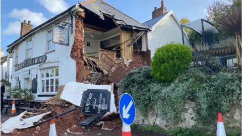 BBC Pub with wall missing and collapsed on the road