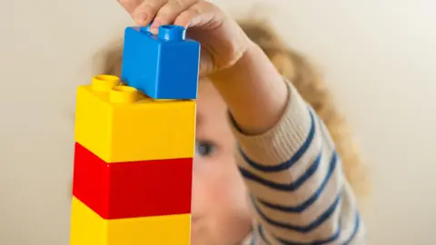 A pre school child is stacking yellow and red building blocks