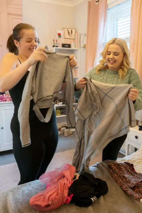 Durham County Council Ms Weatherstone (left) and Ellie sorting clothes in a bedroom. Ms Weatherstone is holding a black-and-white striped top, which Ellie is holding a grey blanket. Other items of clothing are on the bed.