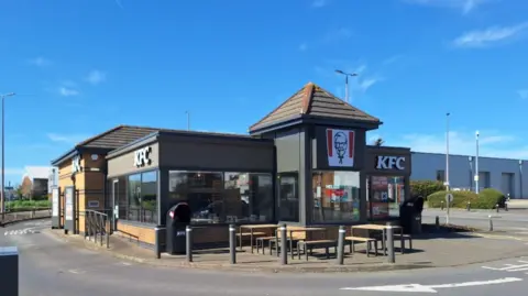A KFC building with seating outside and bollards.