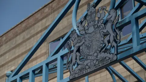 The entrance to Wolverhampton Crown Court. A blue metal frame is above the main door, with blue railings to the left of the shot.