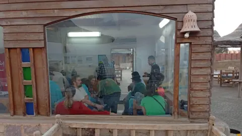 EPA Survivors of the sinking boat rest at the harbour in a building, with a large window through which they can be seen