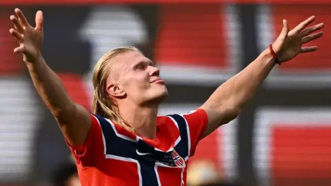 Reuters Erling Haaland in Norway's Red shirt with black cross saltes the fans after scoring against Brazil.