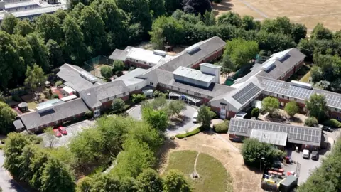 An aerial image of interlinked two storey buildings surrounded by trees