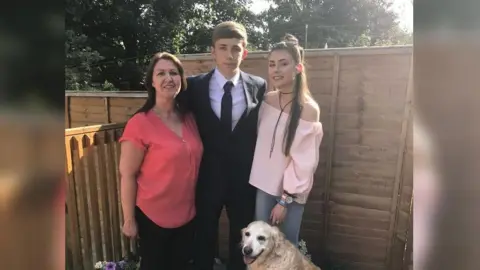 Family handout Maria Britton, wearing a red colour top on the left, Harry Britton, middle in a suit and Emily on the right, wearing a pink off shoulder jumper. Their Labrador is also in the picture at the bottom.