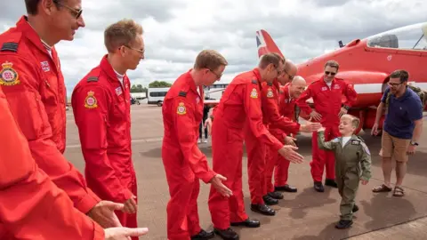 Crown Copyright Little boy high-fiving Red Arrows crew on a flight line