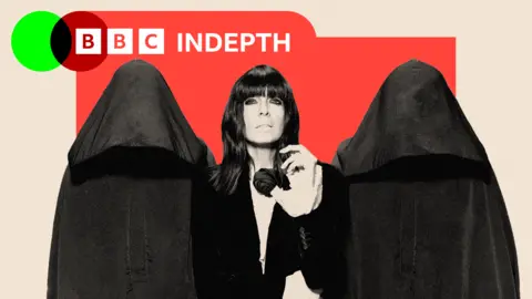 Two hooded figures are by the sides of Traitors host Claudia Winkleman