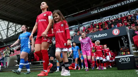 Getty Images Players from Bristol City and Durham's women's walk out of the players' tunnel at Ashton Gate Stadium, some of the players hand in hand with young mascots. Bristol City players are in red and white and the Durham players are in their kit of blue and white