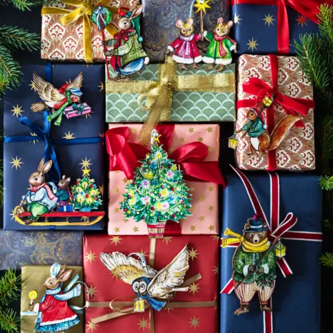 Amy Swann/Fortnum and Mason A collection of nine wrapped Christmas presents with labels featuring designs including rabbits, an owl, a bear, mice and robins. Some are in winter clothing. There are Christmas trees and presents on some of the labels. All are brightly coloured.