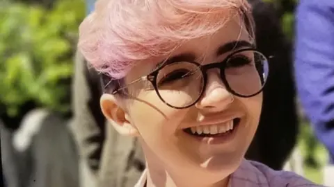 Family handout A woman with short pink hair, glasses and wearing a pink shirt.