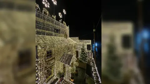 A house completely covered in warm white Christmas lights. Lights are also draped all over the trees in the front garden.