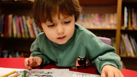 Getty Images A little boy uses a colouring book with a bookcase behind him