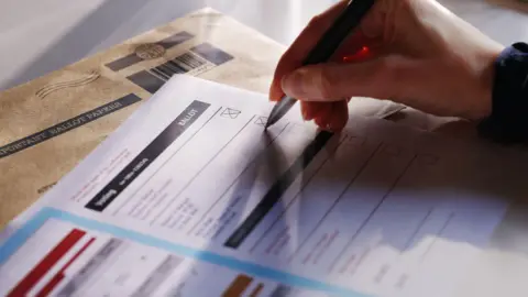 Generic image of a hand writing on a ballot card which is out of focus.