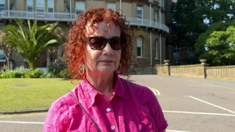 Joanna Bury in a pink top and wearing sunglasses, standing in gardens outside Bournemouth Town Hall