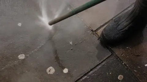 A jet washer spraying the pavement that has chewing gum stuck on it