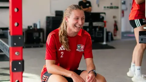 Exeter City Football Club Bow Jackon wearing a red football shirt, hunched in a gym setting with a big smile on her face