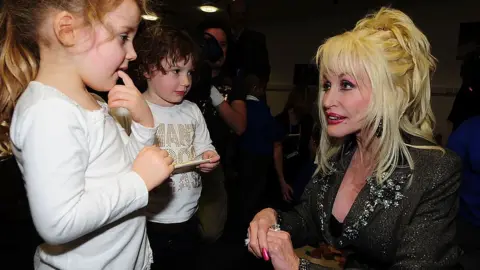 Dolly Parton crouches down to speak to two young children