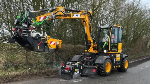 Ollie Conopo/BBC Yellow machine resembling digger with its claws raised on a road