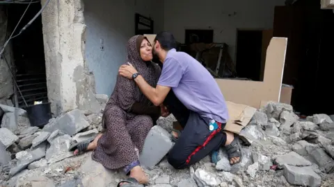 Reuters A Palestinian woman is kissed by her son after returning to their destroyed house following Israel- Hamas truce, in Beit Hanoun in the northern Gaza Strip, May 21, 2021.