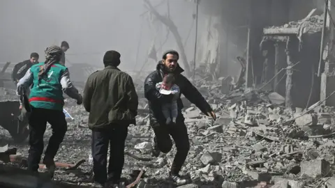 Syrian man carries an infant injured in government bombing in the besieged Eastern Ghouta region of Damascus