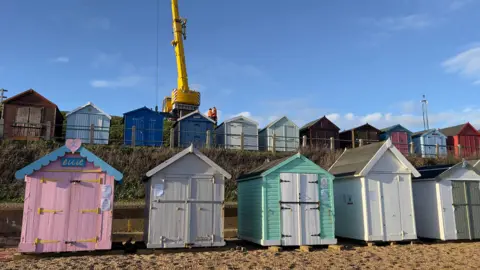 John Fairhall/BBC A crane lifting up one of the beach huts at Felixstowe beach