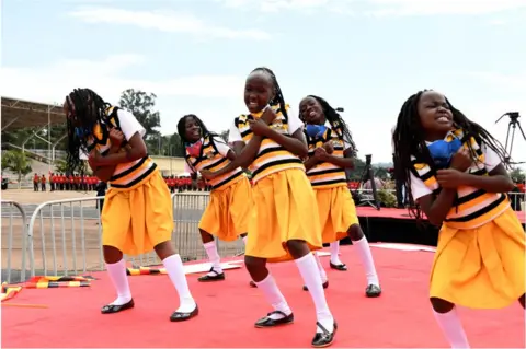 Getty Images Group of girls dressed in yellow dancing on a red carpet.