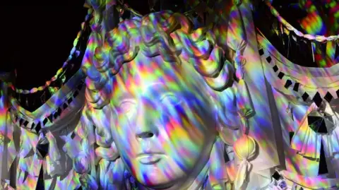 Fountains Abbey A close-up of a face sculpture with multicoloured lights reflected on it.