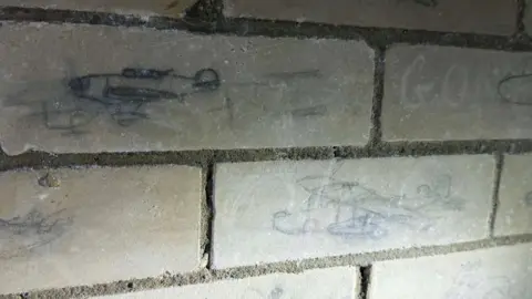Steve Ladner/BBC Some of the war graffiti still seen in the tunnels today. Aircrafts have been drawn on the bricks.