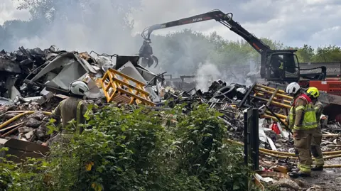 Eric Johnson/BBC A close up of the firefighters inspecting the scrap metal that is alight. Hoses used to tackle the blaze remain on the ground. 