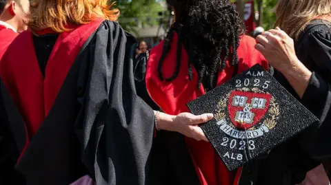 Students attend Harvard University's graduation ceremony and one holds a decorated graduate's cap.
