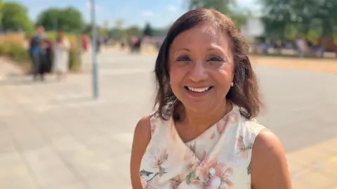 A woman with shoulder length dark hair, wearing a floral top, smiles at the camera