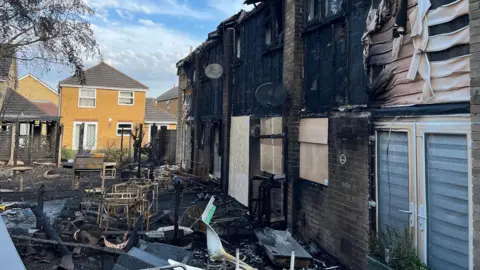 George Carden/BBC A house destroyed by fire. There are debris lying around the garden.
