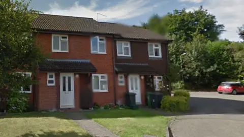 A two-storey, end-of-terrace house with a lawn in front and a small car park beside it.