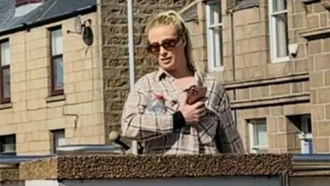 BBC Sophie-Leigh Gemmell outside the court. She is wearing sunglasses and a checked shirt and carrying a mobile phone