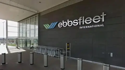 Google Interior of Ebbsfleet International stations with a big Ebbsfleet sign on the wall in silver and silver barriers and a big glass window at the rear