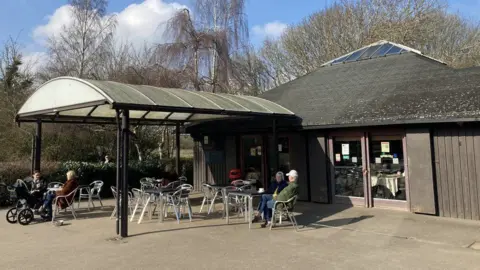 The exterior of the cafe space at the country park. There is an awning above metal chairs and tables outside.