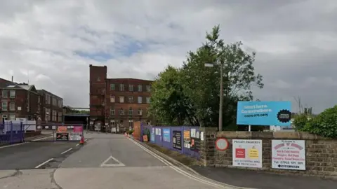 LDRS An entrance to an industrial estate with a large mill building seen in the background. 
