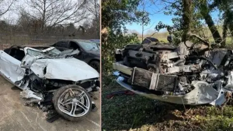 Submitted Two photos next to each other showing the wreckage of a car. On the right is a white overturned car positioned on a woodland floor next to several trees and a fence and field behind it. It is severely damaged. On the left the same car is upright and parked on concrete, with the front shown to be severely damaged. The window is pressed in and a wheel has come off it.